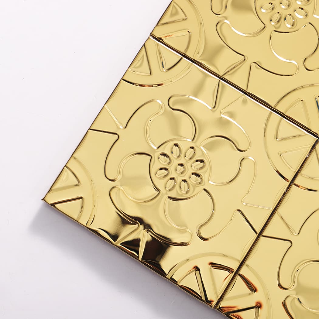Corner close-up of gold embossed metal mosaic tile showing raised floral details.