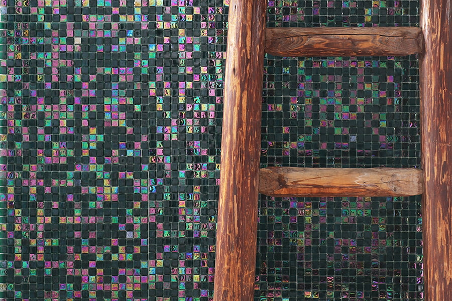 Green iridescent mosaic tiles with a wooden ladder leaning against the wall 