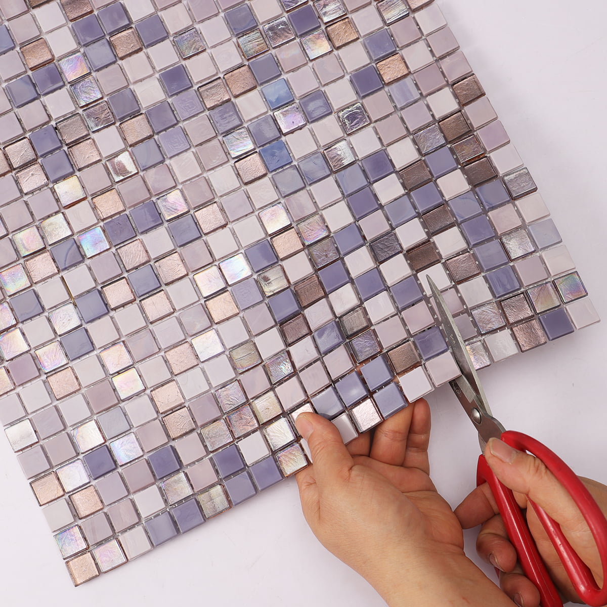 Hand cutting iridescent mosaic tile sheet with scissors