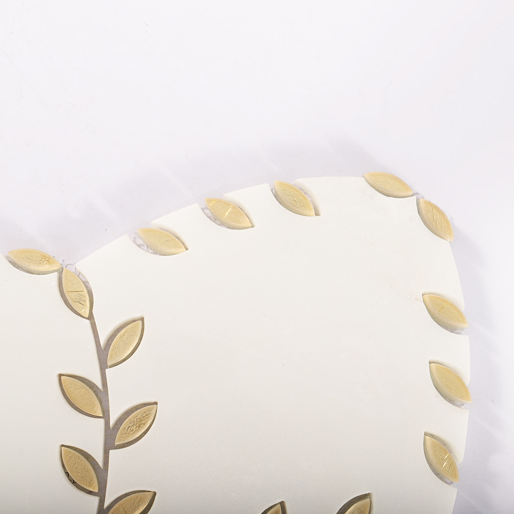 Close-up of the top edge of a marble tile decorated with gold leaf shapes.