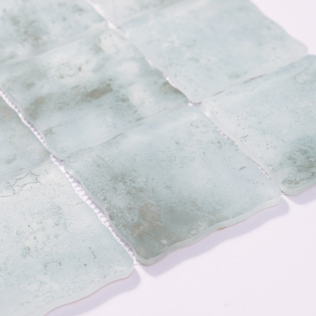 Edge detail of pale aqua wavy square glass mosaic tiles on mesh