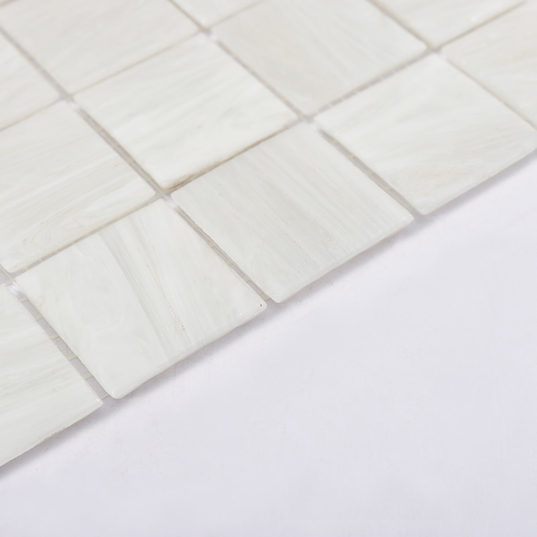 Edge detail of pearl white glass mosaic tiles with grout gaps on a white background