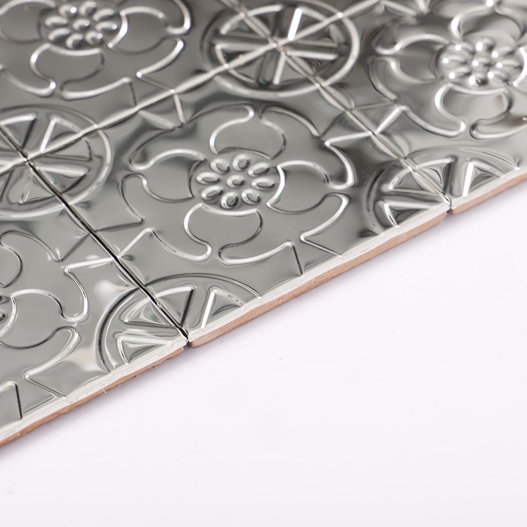 Side angle view of silver embossed flower mosaic tile sheet showing raised pattern and edges.