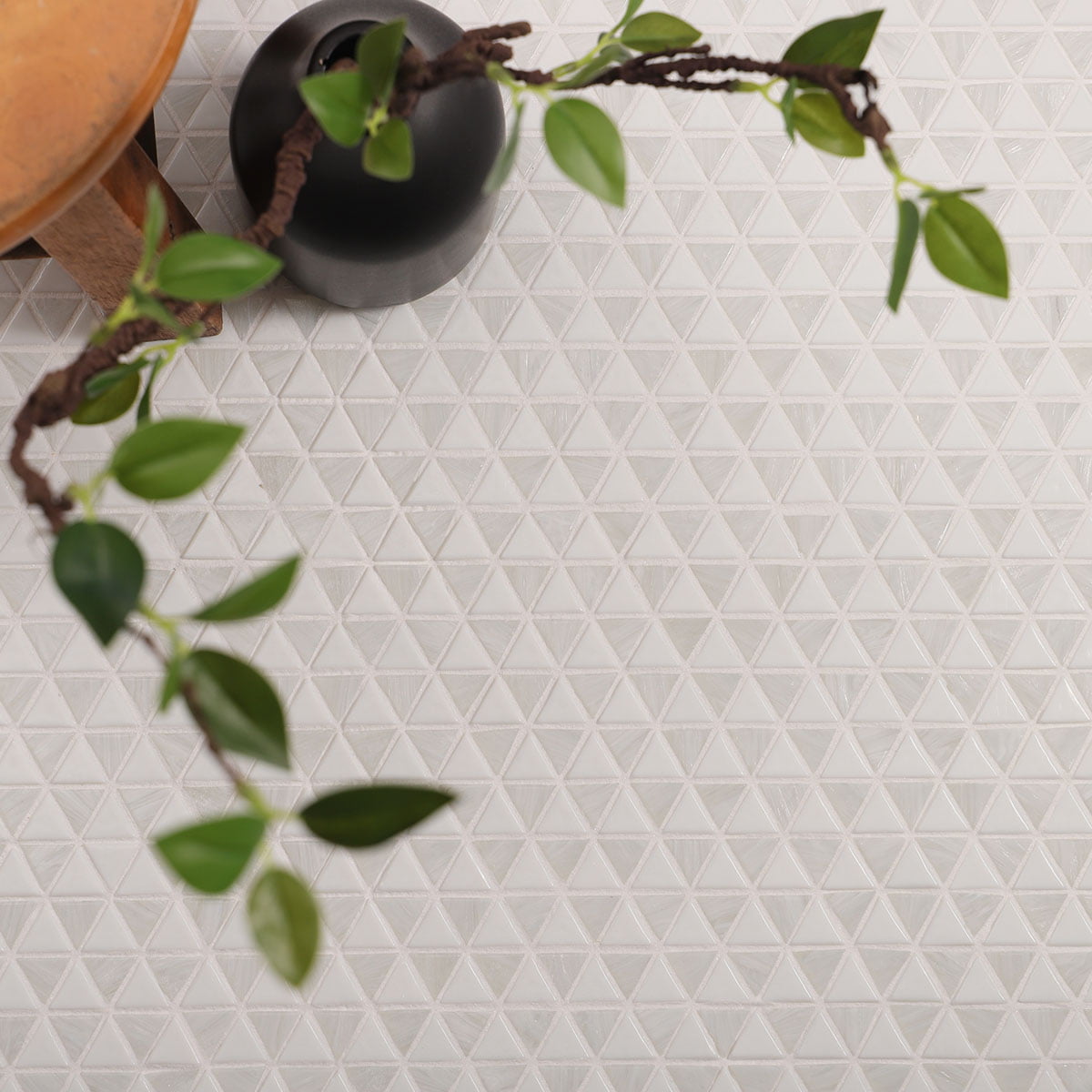White triangular mosaic tiles on a floor, paired with greenery and minimalist decor