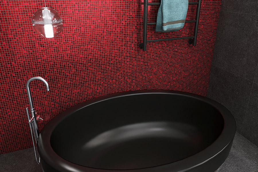 Angled view of black bathtub on gray floor against red mosaic wall and towel warmer