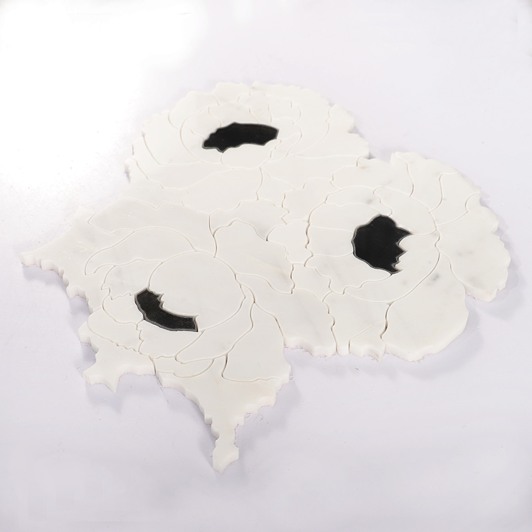Angled view of white marble flower mosaic tile sheet with black centers.