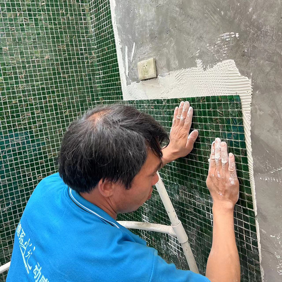 Worker pressing green mosaic tile sheet onto wall with adhesive.