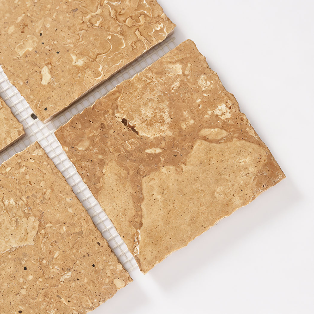Close-up of beige marble mosaic squares with fossil patterns and uneven edges
