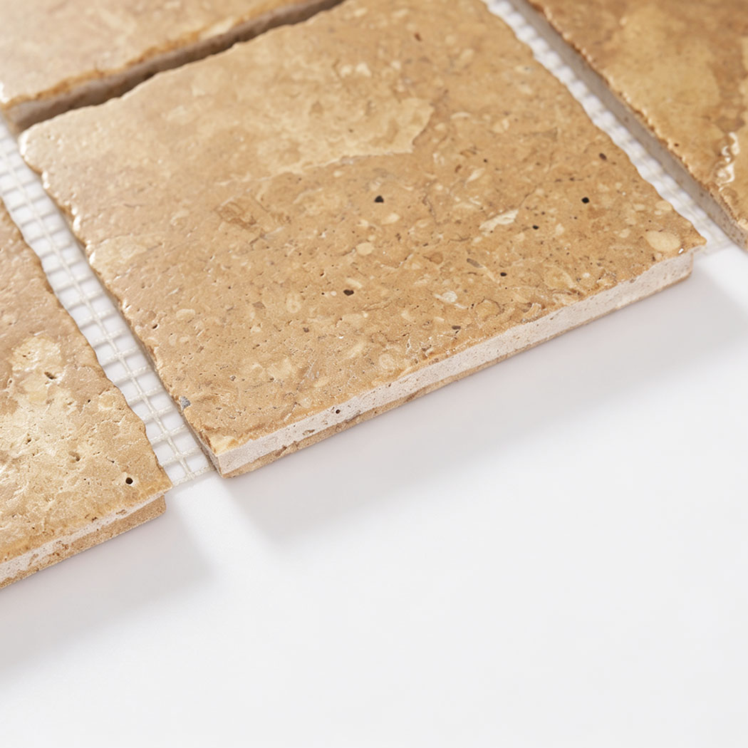 Angled close-up showing the textured surface and thickness of beige marble tile