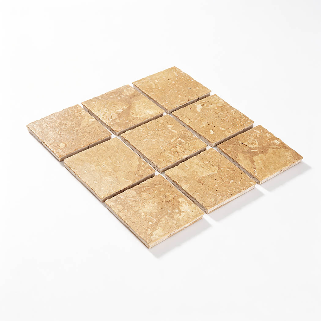Angled view of nine beige square marble pieces arranged on a mosaic sheet