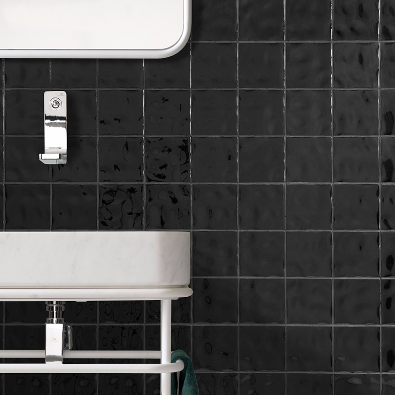 Glossy handmade black square tiles on a modern bathroom wall