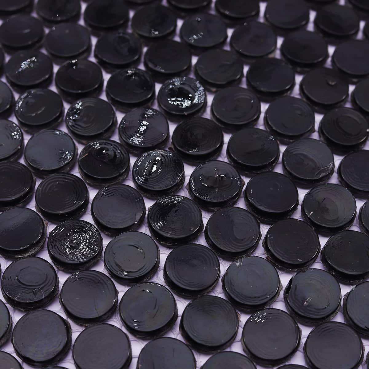 Angled close-up of glossy black round mosaic tiles with light reflection