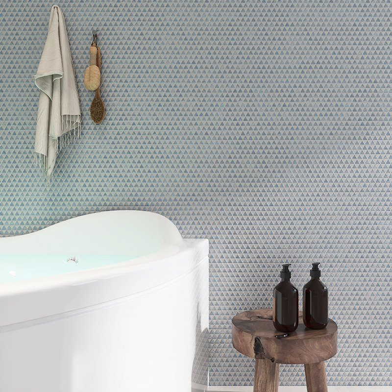 Blue glass triangle mosaic tiles on a bathroom wall behind a white bathtub