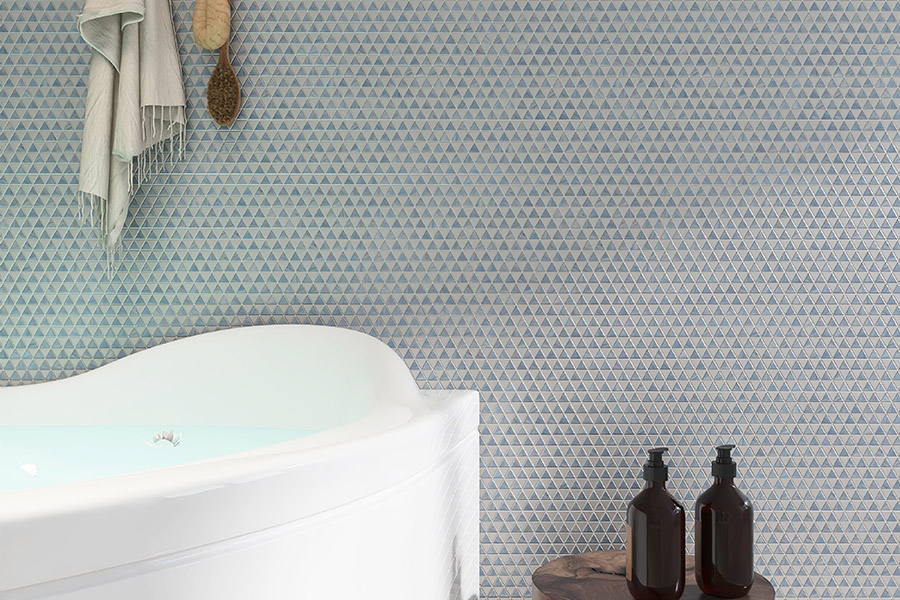 Blue glass triangle mosaic tile bathroom wall with a white bathtub and decor bottles