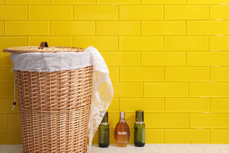 Bright yellow long subway tiles wall with wicker basket and bottles on speckled counter