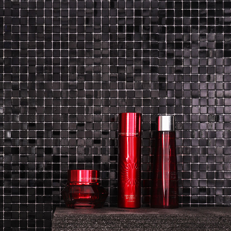 Black mosaic tiles on the wall with red cosmetics in front.