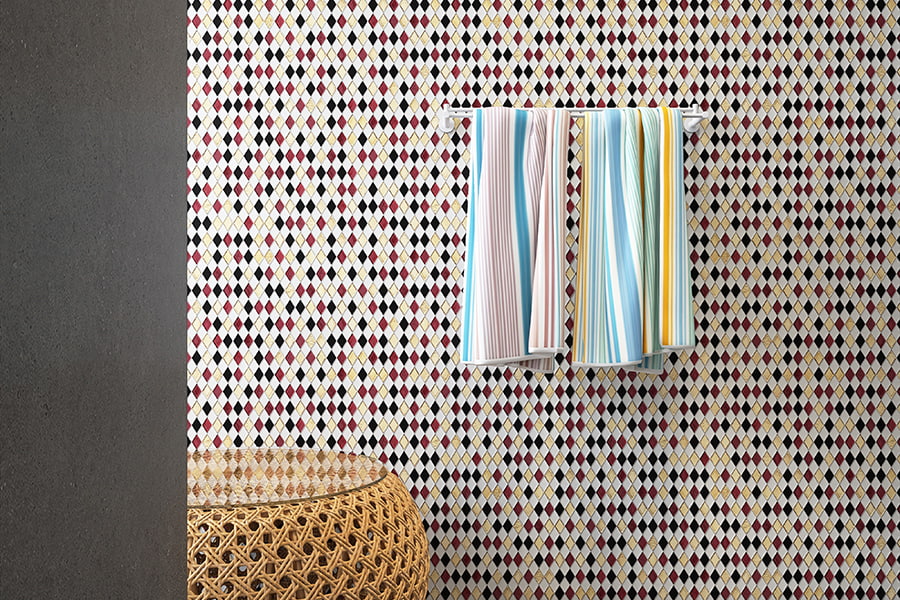 Diamond-patterned glass mosaic tile wall in black, red, white, and gold with hanging towels