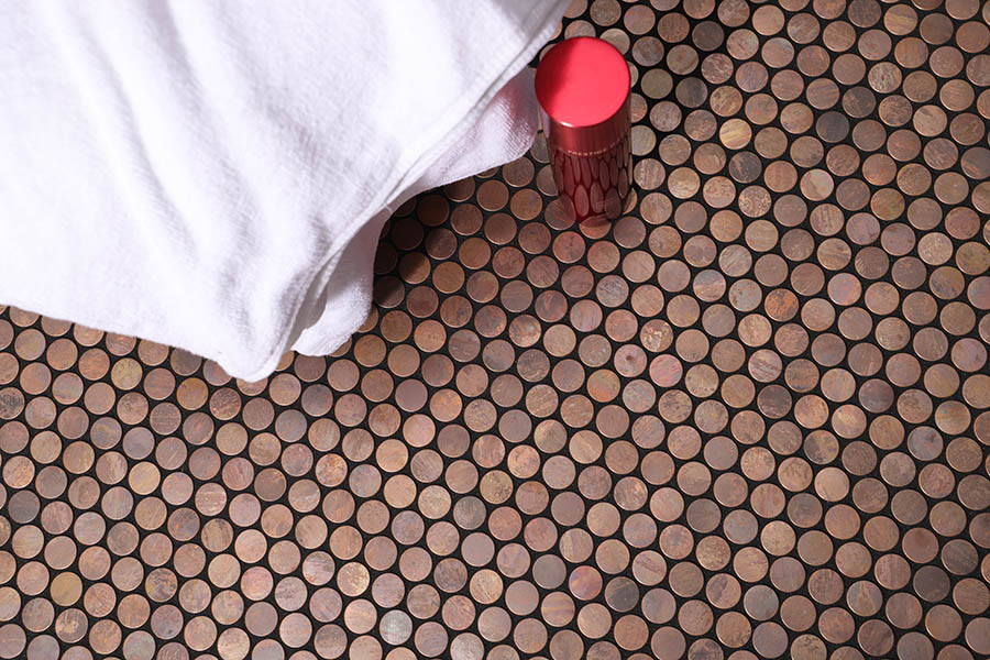 Copper penny tile bathroom floor scene with white towel and red bottle