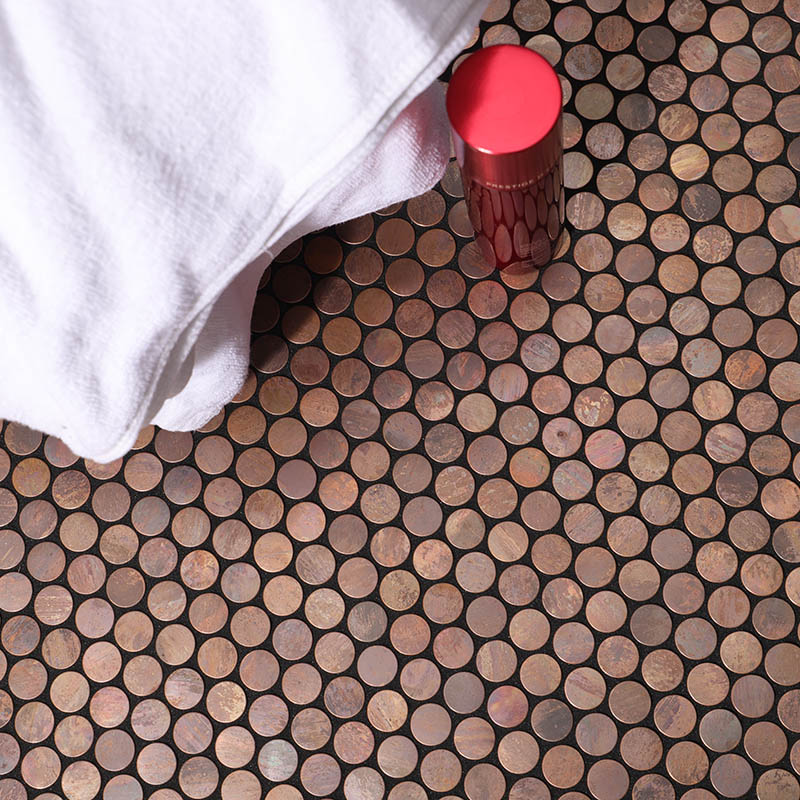 Copper penny tile floor close-up with white towel and red bottle