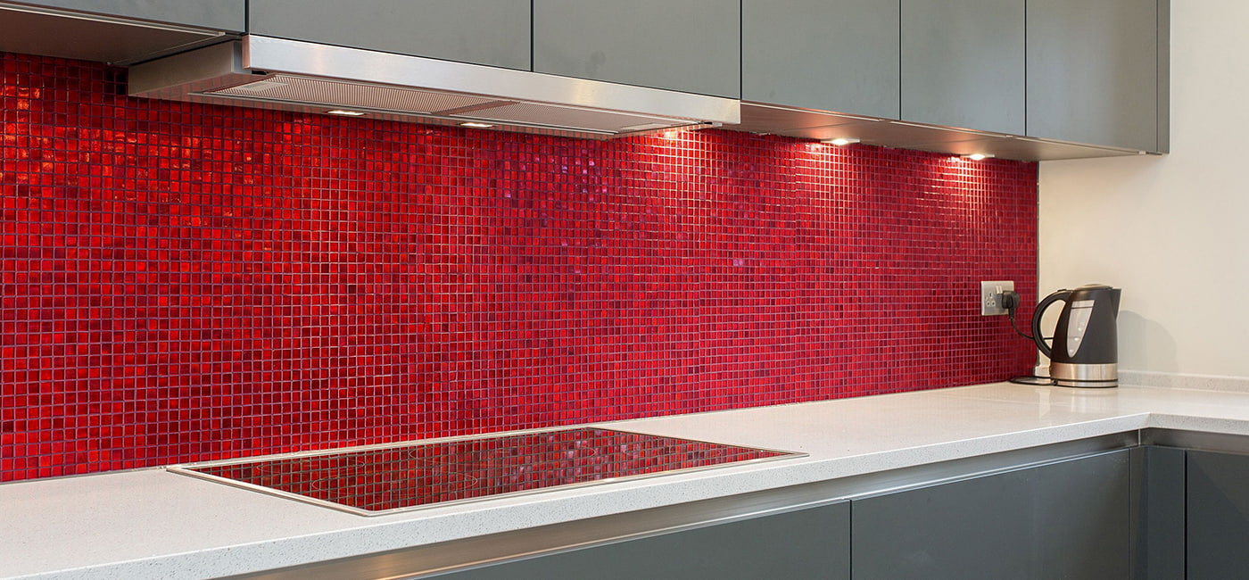 Red glass mosaic tile backsplash wrapping around kitchen corner under grey cabinets 