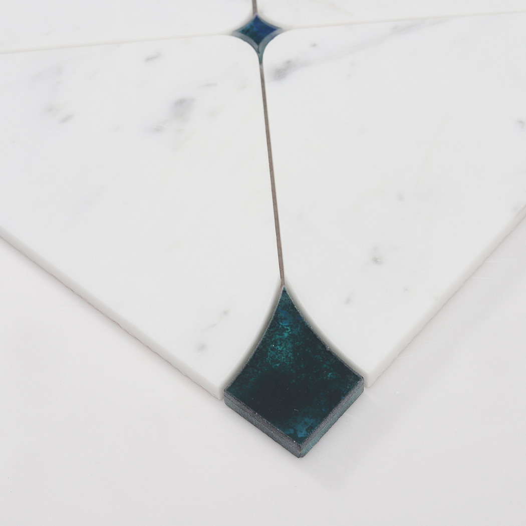 Angled close up showing the texture and thickness of a teal glass corner inlay on a marble tile.