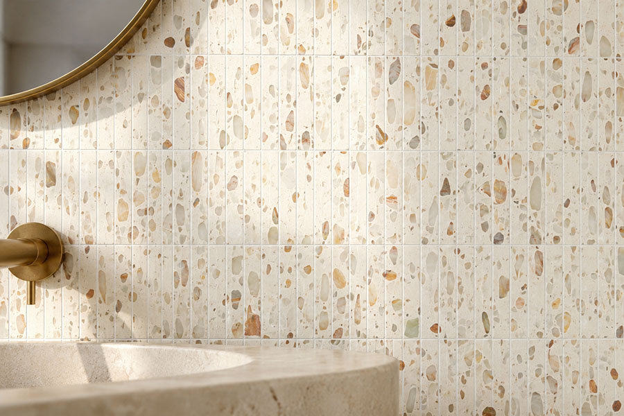 Cream vertical terrazzo mosaic bathroom wall with a stone sink, round mirror and brass faucet