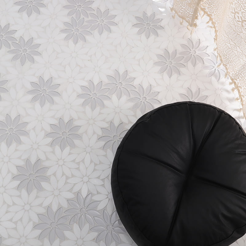 White daisy mosaic tiles with gray floral pattern on floor featuring black round cushion