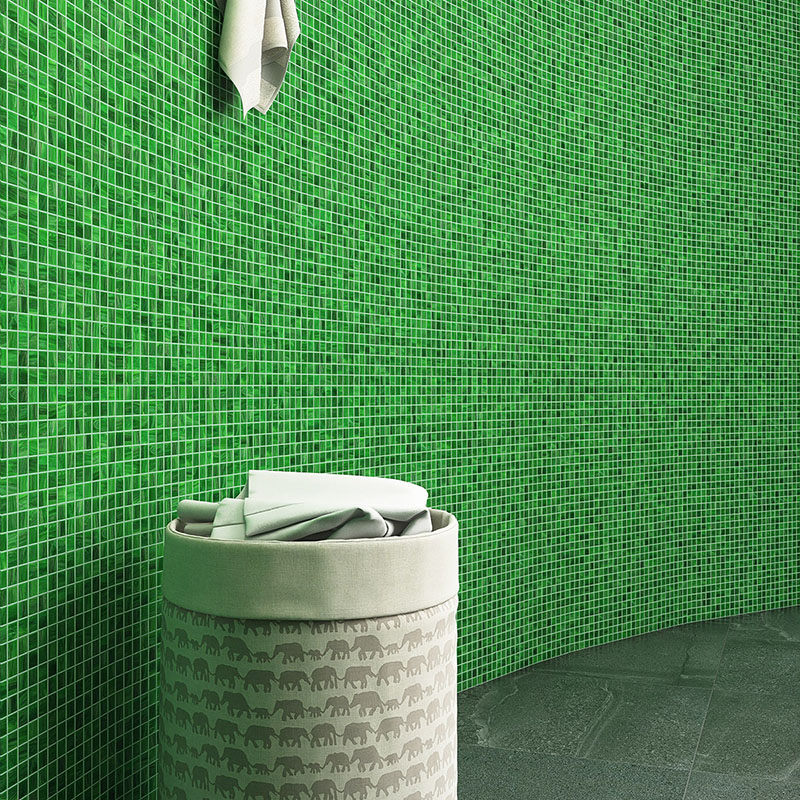 Emerald green glass mosaic tiles cover a bathroom wall beside a towel basket.