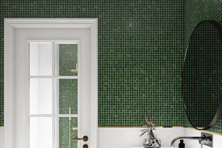 Forest green glass mosaic tiles on a bathroom wall with gold trim and a white door.