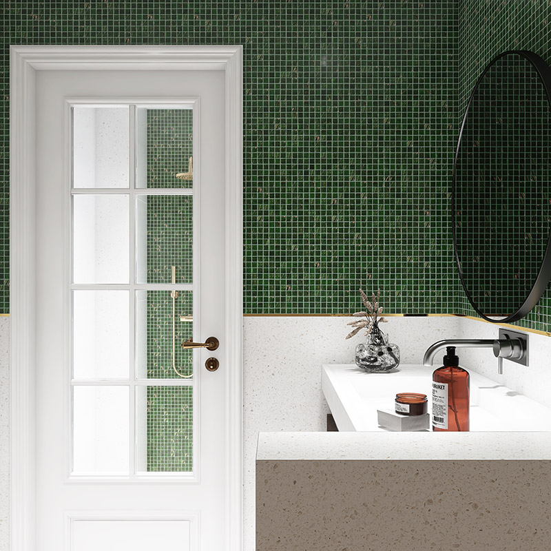 Modern bathroom featuring forest green tiles, gold accents, and a round black mirror.