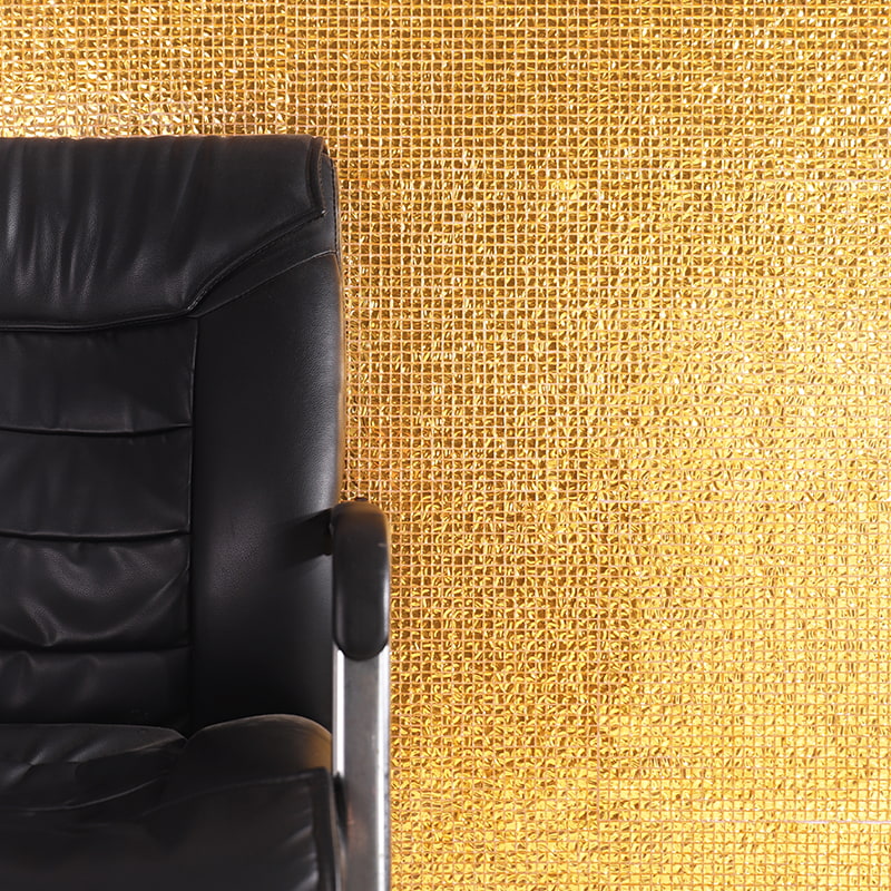 Metallic gold glass mosaic tile wall with foil-backed texture behind black leather chair
