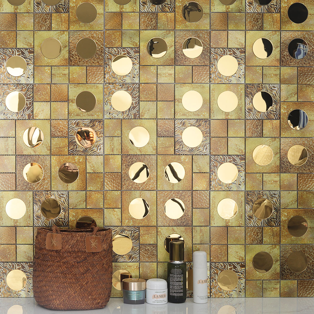 A bathroom wall with gold mosaic tiles featuring skincare products on the counter.