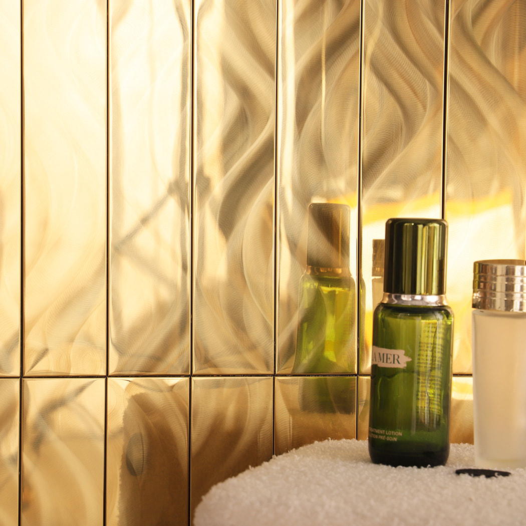 Close up of gold stainless steel wave mosaic wall reflecting light and bottles.