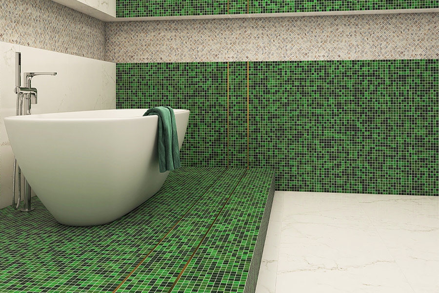 Modern bathroom with green mosaic tiles on the floor and walls, featuring a white freestanding tub.