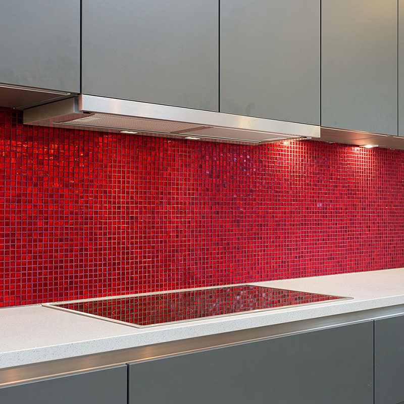 Red glass mosaic tile backsplash illuminated by under-cabinet lights above stovetop
