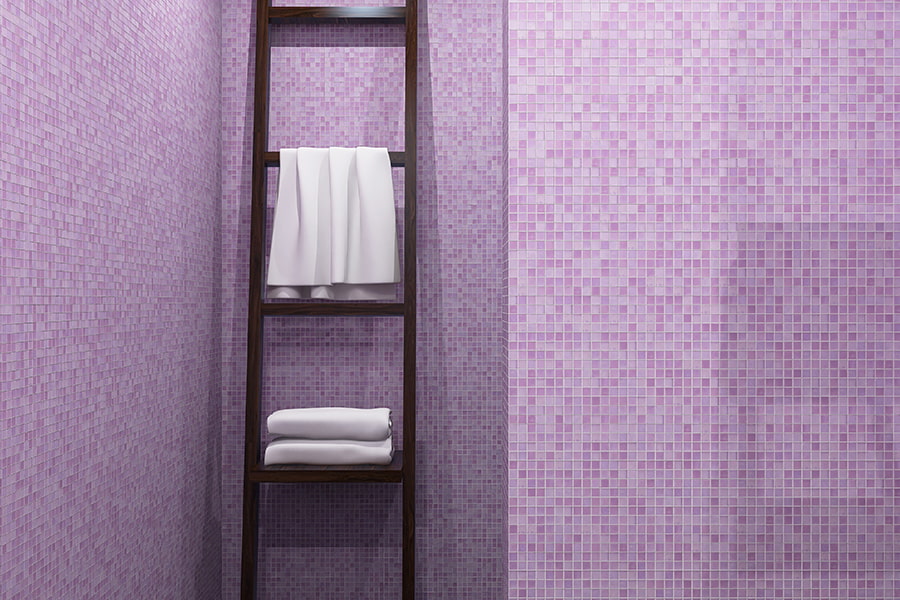Close-up view of lavender glass mosaic wall and wooden towel ladder with folded towels
