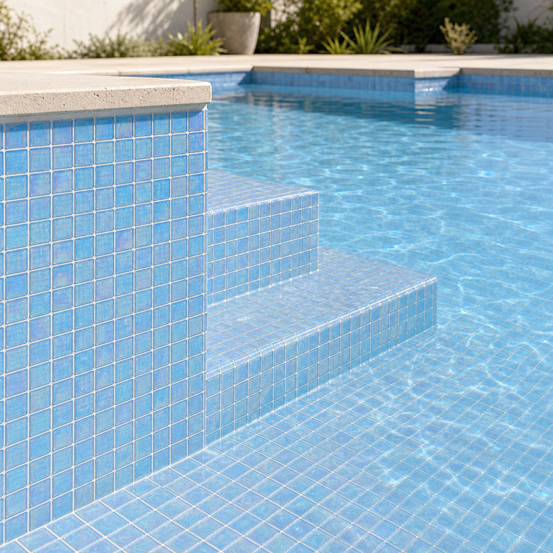 Light blue 1x1 iridescent glass pool tiles on steps and raised spa wall