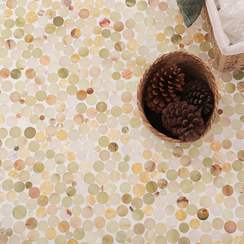 Close-up of mixed-size light green and cream round mosaic floor tiles beside a pinecone basket