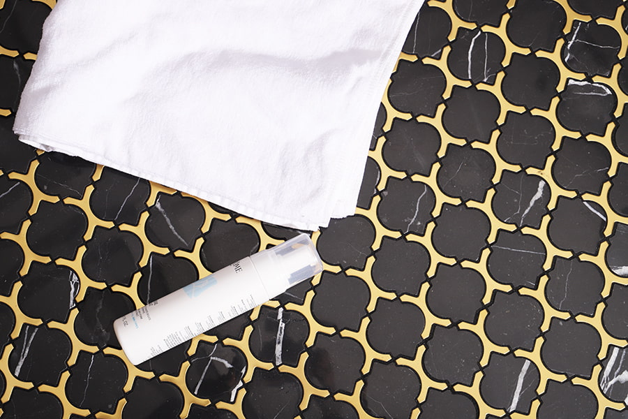 Luxury black marble arabesque floor tiles with gold grout, towel and skincare bottle