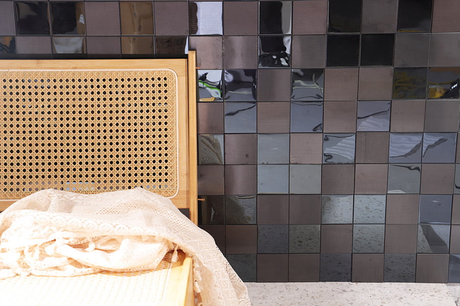 Dark square metal wall tiles with reflective surface and wooden chair in front