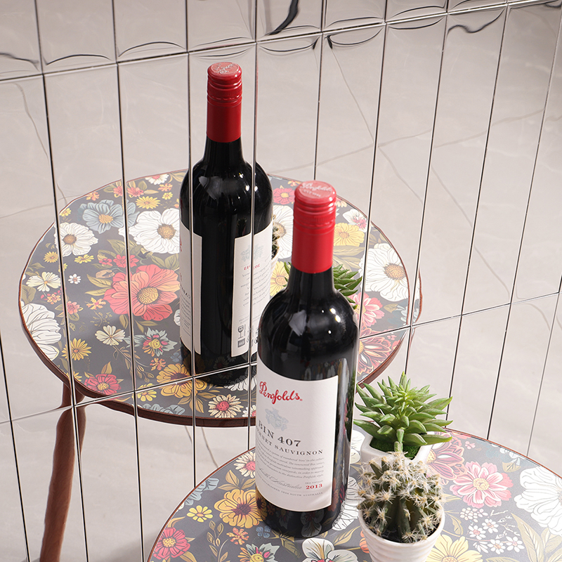 Mirror mosaic tiles reflecting a wine bottle on a floral table with small succulents.