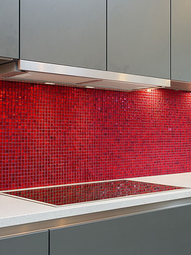 Close-up of vibrant red glass mosaic backsplash against a white quartz countertop