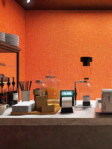 A vibrant orange glass mosaic backsplash behind a marble countertop with coffee accessories