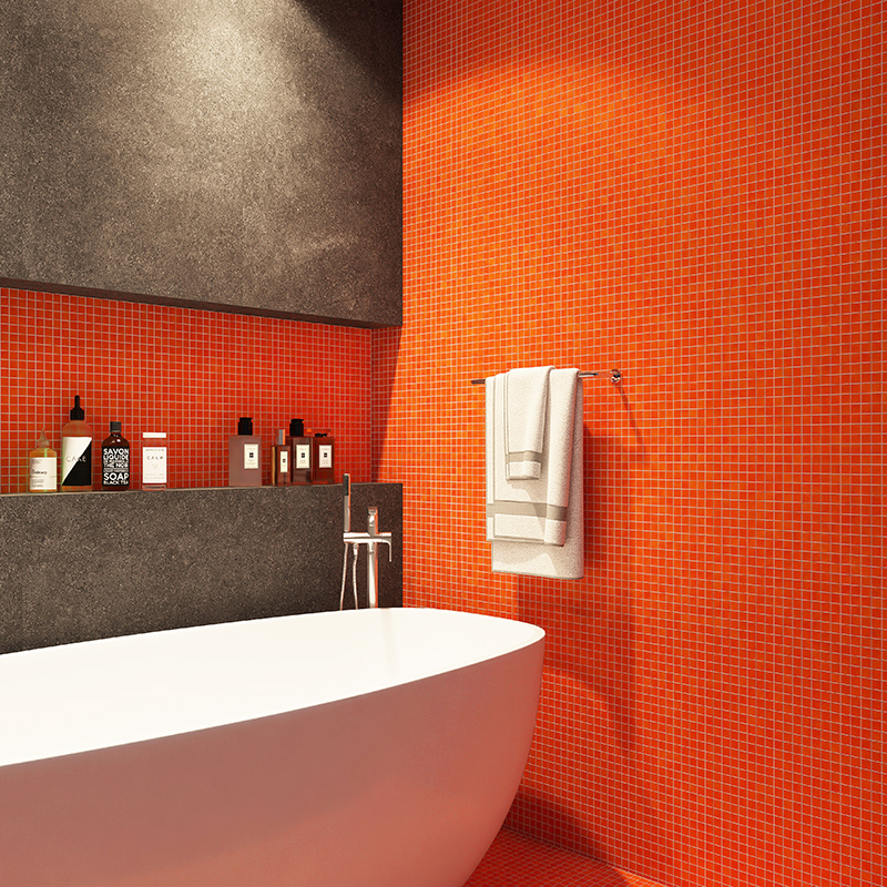 Bathtub against vibrant orange mosaic tile wall with towel bar and dark stone accent shelf