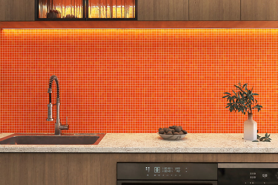 Modern kitchen wall featuring vibrant orange mosaic tiles above marble countertop and stainless sink