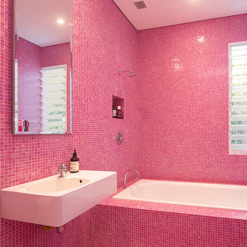 Contemporary pink glass mosaic bathroom with wall-mounted sink, mirror, and recessed shower niche