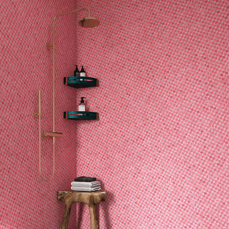 Pink glass mosaic shower wall with gold-tone fixture and teak stool