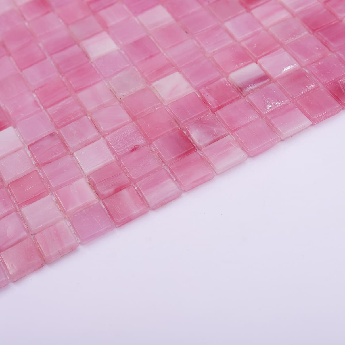 Angled side view of light pink square glass mosaic tiles with seamless finish