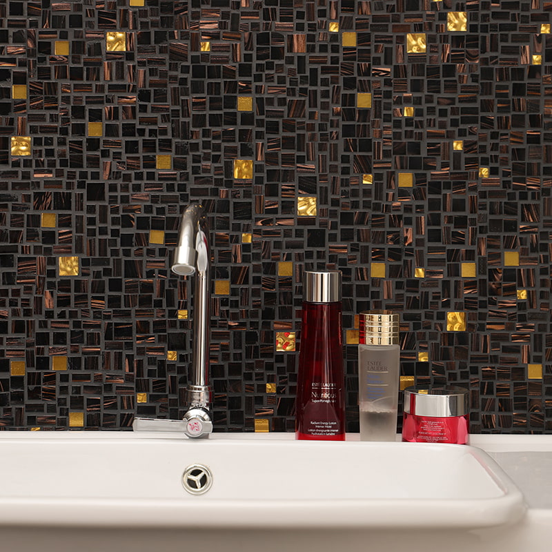 Dark random glass mosaic tiles with gold accents behind a bathroom sink