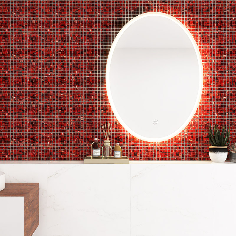 Red backsplash tiles in a glass mosaic pattern with an illuminated oval mirror.